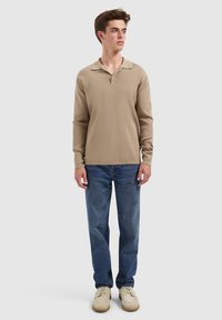Beige polo shirt met lange mouwen en een kraag, gecombineerd met blauwe rechte jeans en beige schoeisel. Eenvoudig ontwerp, minimale textuur.