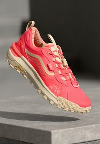 Coral pink athletic shoe with textured mesh upper, padded collar, and tan rubber outsole featuring aggressive traction lugs for grip.