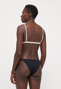 Black bikini set with a textured bottom and white adjustable straps. Features gold-tone hardware for fastening.