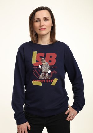 Námořnická modrá mikina s grafickým designem a kreslenou postavičkou na kolečkových bruslích, tučný text a žluté akcenty. Měkká textura.
