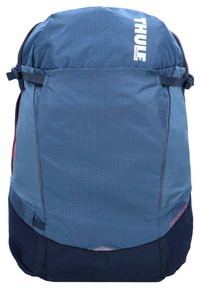 Mochila Thule de tela azul con un patrón geométrico, con una parte superior redondeada, correas ajustables y bolsillos de malla laterales.