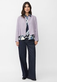 Lavendelcroppad jacka över en mönstrad blus med blå, marinblå och krämfärgade virvlar; tillsammans med vida mörk denimbyxor.