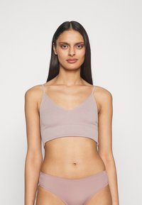 Bralette côtelée rose clair avec des bretelles fines réglables et un décolleté en V. Texture lisse avec une coupe ajustée, accompagnée de culottes assorties.