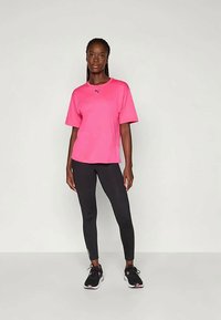 Ružové športové tričko s krátkym rukávom a okrúhlym výstrihom, s čiernym logom, skombinované s čiernymi legínami a čiernymi teniskami s ružovými akcentmi.