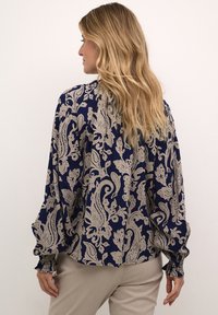 Laivaston sininen paita, jossa on vaaleanbeige paisley-kuvio, pitkät hihat elastisilla resoreilla, pehmeä tekstuuri ja hieman löysä istuvuus.