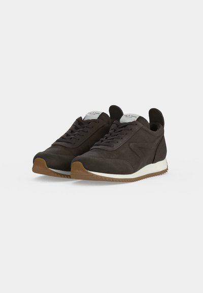 Paire de baskets en daim brun foncé avec des semelles intermédiaires blanches et des semelles en caoutchouc naturel, présentant un laçage frontal et des languettes à l’arrière.
