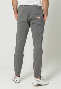 Pantalones deportivos de algodón grises con cintura elástica, puños estrechos, bolsillo trasero y etiqueta de marca, combinados con zapatillas blancas.