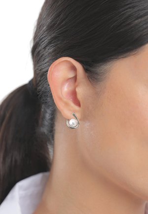 Frauenohr mit dunklem, zurückgebundenem Haar, trägt einen silbernen Ohrring mit rundem Design und einer einzelnen weißen Perle.