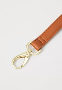 Cinturino in pelle marrone con clip in metallo dorato. Texture liscia, dettagli di cucitura prominenti lungo i bordi. Design funzionale e durevole.