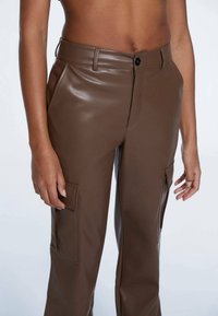 Bruine neplederen cargobroek met hoge taille, sluiting met knoop aan de voorkant en zijzakken. Soepele textuur met een lichte glans.