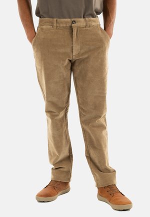 Pantalon en velours côtelé beige avec une coupe droite, doté d'une fermeture à bouton et de poches latérales, associé à des chaussures à lacets marron.