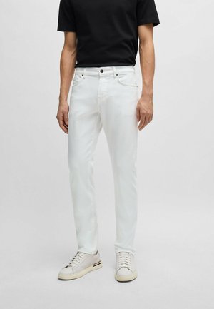 Jeans in denim bianco con cinque tasche, chiusura frontale con bottone, vestibilità slim e superficie liscia, abbinati a sneakers chiare e a una t-shirt nera.
