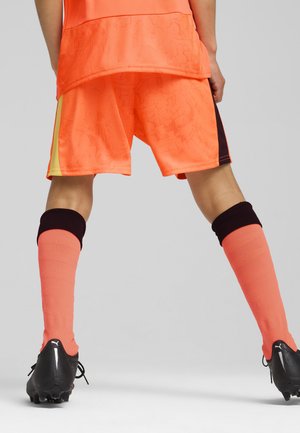 Klarr orange sportströja och shorts med ett strukturerat mönster, tillsammans med knä-långa orange strumpor och svarta fotbollsskor.