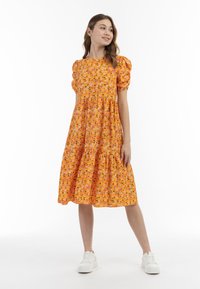 Oranges Blumen-Midi-Kleid mit Puffärmeln, gestuftem Rock und weißen Sneaker-Elementen. Das Kleid ist mit kleinen, bunten Blumen auf dem Stoff bedruckt.