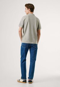 Polo gris �à manches courtes, associé à un jean bleu et des baskets blanches. Le polo a un col classique et une texture lisse.