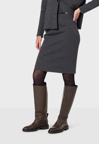 Jupe crayon en tricot gris associée à des bottes en cuir marron hauteur genou, avec un design ajusté et un tissu texturé, complétée par des collants noirs.