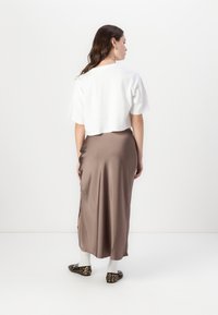 Hvit cropped t-skjorte, lys brun satin skjørt med sidesliss, dyreprint leilighetssko og hvite sokker. Enkelt design, glatt tekstur.