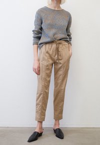 Gebreide blauwe en bruine trui met een losse pasvorm, gecombineerd met beige tapered broeken met zijklinkers en een verstelbare taille. Zwarte mules.