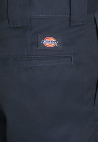 Dark blue Dickies pants featuring a visible leather logo patch, smooth fabric texture, and a flat back pocket design with minimal stitching.