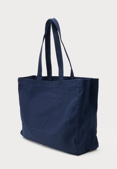 Navy blue canvas tote bag with two long handles and a square patch detail on the front, standing upright on a plain background.