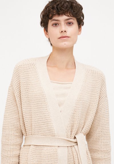 Beige knitted cardigan with a textured weave, open front, and matching tie belt at the waist. The design features a V-neck and long sleeves.