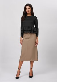 Top negro de manga larga con un dobladillo acampanado, combinado con una falda beige hasta la rodilla. La modelo lleva unos tacones negros de punta. Texturas de tela suaves.