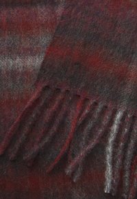 Sciarpa di lana in tonalità di rosso, nero e grigio con una consistenza morbida; presenta frange lunghe a un'estremità e un sottile motivo a tartan.