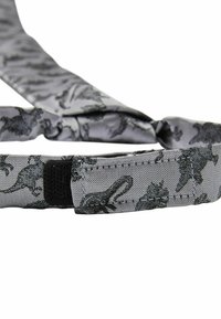 Cravate en tissu gris avec un motif de dinosaures noirs, dotée d'une surface texturée et d'une fermeture velcro. Le design inclut diverses silhouettes de dinosaures.