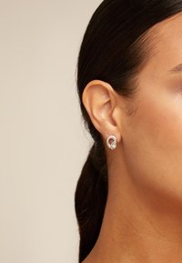 Boucles d'oreilles en argent en forme de créole, dotées d'un petit accent ovale avec une pierre centrale, sur un teint de peau neutre et des cheveux foncés.