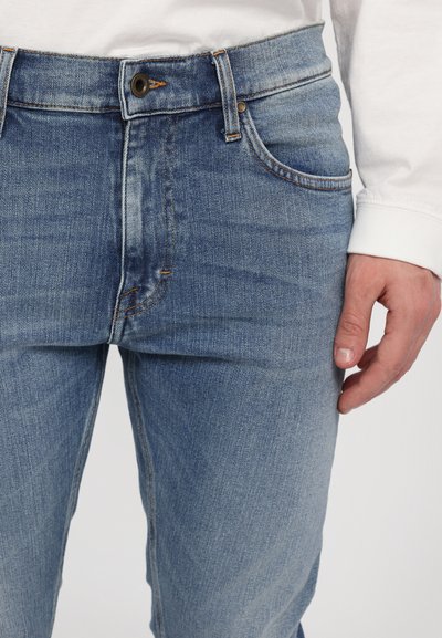 Blauwe spijkerbroeken hebben een klassiek ontwerp met een rechte pasvorm. De stof heeft een gewassen uiterlijk en er zijn metalen accenten op de taille.