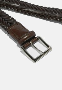 Flettet brun læderbælte med en glat finish og en sølv metal spænde. Har et vævet mønster langs stroppen og syede detaljer.