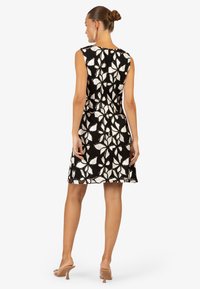 Robe à motifs floraux en noir et blanc avec un design sans manches, longueur au-dessus du genou et taille cintrée. Texture lisse et légère brillance.