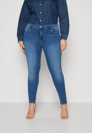 Jeans skinny blu con un lavaggio sbiadito. Presentano un classico design a cinque tasche con cuciture visibili e una zip. Il modello è abbinato a tacchi beige.