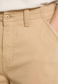 Pantalons en coton kaki avec une texture lisse, dotés d'une fermeture à bouton, de cinq poches et d'une coupe droite.