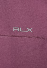 Lila Sportbekleidungsstoff mit einer glatten Textur, einer genähten Naht und einem auffällig platzierten silbernen "RLX"-Logo.