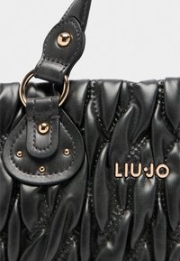 Borsa a tracolla nera trapuntata realizzata in pelle morbida e testurizzata, con hardware color oro, logo prominente e una tracolla decorativa con dettagli a forma di anello.
