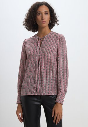 Blusa a maniche lunghe con motivo rosso e bianco, con scollo rotondo e chiusura a bottoni. Realizzata in un tessuto leggero con una texture liscia.