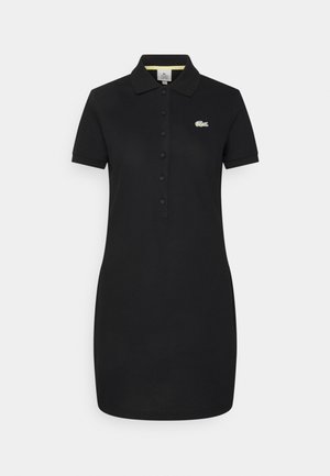Vestido polo negro de manga corta con cuello, tapeta de botones y pequeño logo de cocodrilo verde en el pecho izquierdo.