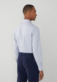 Camicia azzurro chiaro a fantasia con una texture morbida, abbinata a pantaloni blu scuro. La camicia presenta un colletto classico e polsini con bottoni.
