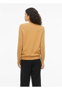 Heled pruun kudumispullover ümmarguse kaelusega, soonikkoes mansettide ja äärisega, kantud mustade pükstega. Omab siledat tekstuuri ja lõdva istuvust.