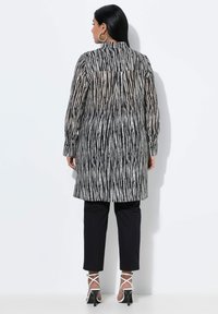 Camicia lunga a righe bianco e nero con colletto alto, polsini con bottoni e tessuto trasparente, abbinata a pantaloni neri e tacchi con cinturino.