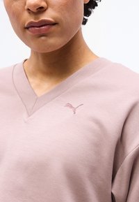 Κοντινό πλάνο ενός ατόμου που φοράει ελαφρύ πουκάμισο σε απόχρωση mauve με V λαιμόκοψη και μικρό κεντημένο λογότυπο Puma στο αριστερό μέρος του στήθους.