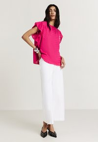 Top rosa a fantasia con maniche a volant, abbinato a pantaloni bianchi a gamba larga e scarpe nere con punta appuntita decorate con borchie argentate.