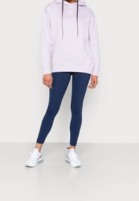 Ljuslila hoodtröja med dragsnören, bärs över marinblå leggings. Vita fitnessskor fulländar looken och betonar en sportig stil.