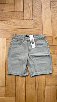 Sivi denim kratke hlače s klasičnim petimi žepi, ravnim krojem in vidnimi šiviljskimi detajli. Priložena je oznaka s QR kodo.