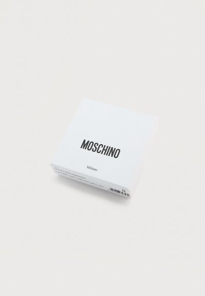 Λευκό κουτί Moschino Milano με μαύρο κείμενο σε ανοιχτό φόντο, ορατό υπό ελαφριά γωνία με γραμμικό κώδικα στο πλάι.