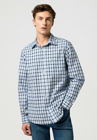 Camicia a maniche lunghe a scacchi blu e bianchi, con colletto button-down e taschino sul lato sinistro, realizzata in un leggero tessuto di cotone misto.
