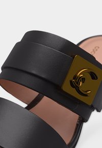 Μαύρο δερμάτινο σανδάλι με φαρδιές λουριά και χρυσή τετράγωνη αγκράφα που φέρει το διαπλεκόμενο διπλό λογότυπο C.