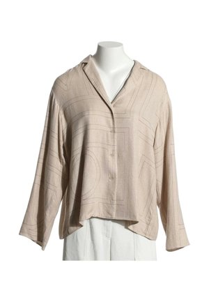 Chemise beige à manches longues avec boutons et motif géométrique subtil sur un buste de mannequin blanc portant un pantalon blanc.