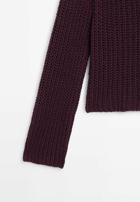 Bordowy sweter z dzianiny o fakturowanym wzorze, z długimi rękawami i luźnym krojem. Materiał wydaje się gruby i przytulny.